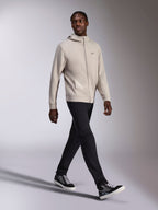 Sweat à capuche Alpinestars Cypher, polaire zippée gris ciment, capuche à col haut, petit logo Astars sur la poitrine, porté par un mannequin en train de marcher, associé à un pantalon noir et des baskets noires et grises, style sportswear décontracté d'inspiration motorsport.
