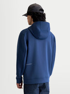 Alpinestars Cypher, sweat à capuche de sportswear bleu acier, vue de dos sur modèle montrant la capuche à col haut et le logo Alpinestars discret sur le bas du dos, polaire premium pour un style motorsport décontracté.