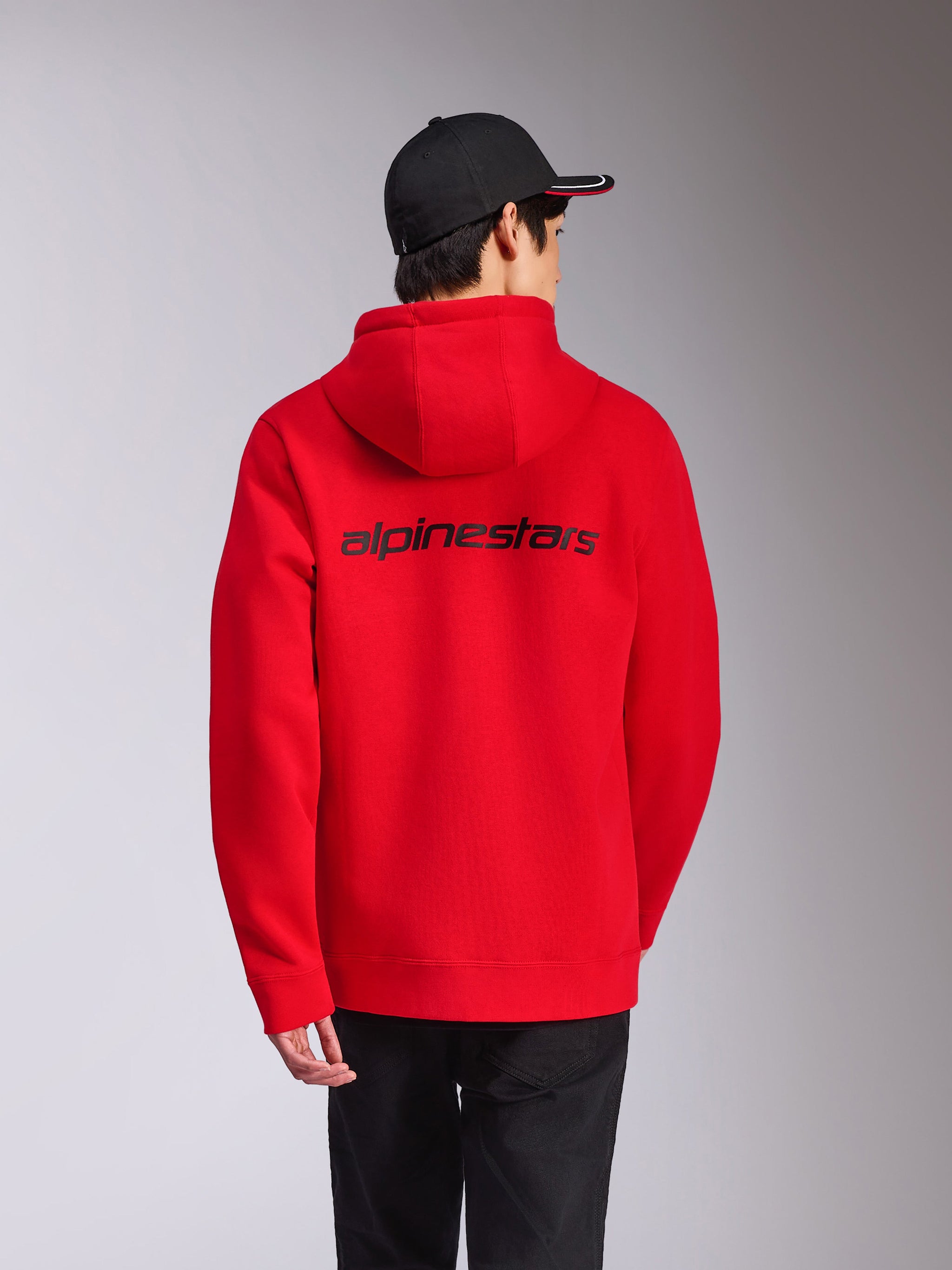 Sweat à capuche Alpinestars Transverse, rouge, vue arrière présentant le logo Alpinestars noir dans le dos, style streetwear décontracté, polaire à capuche avec poignets et ourlet côtelés, porté avec une casquette noire