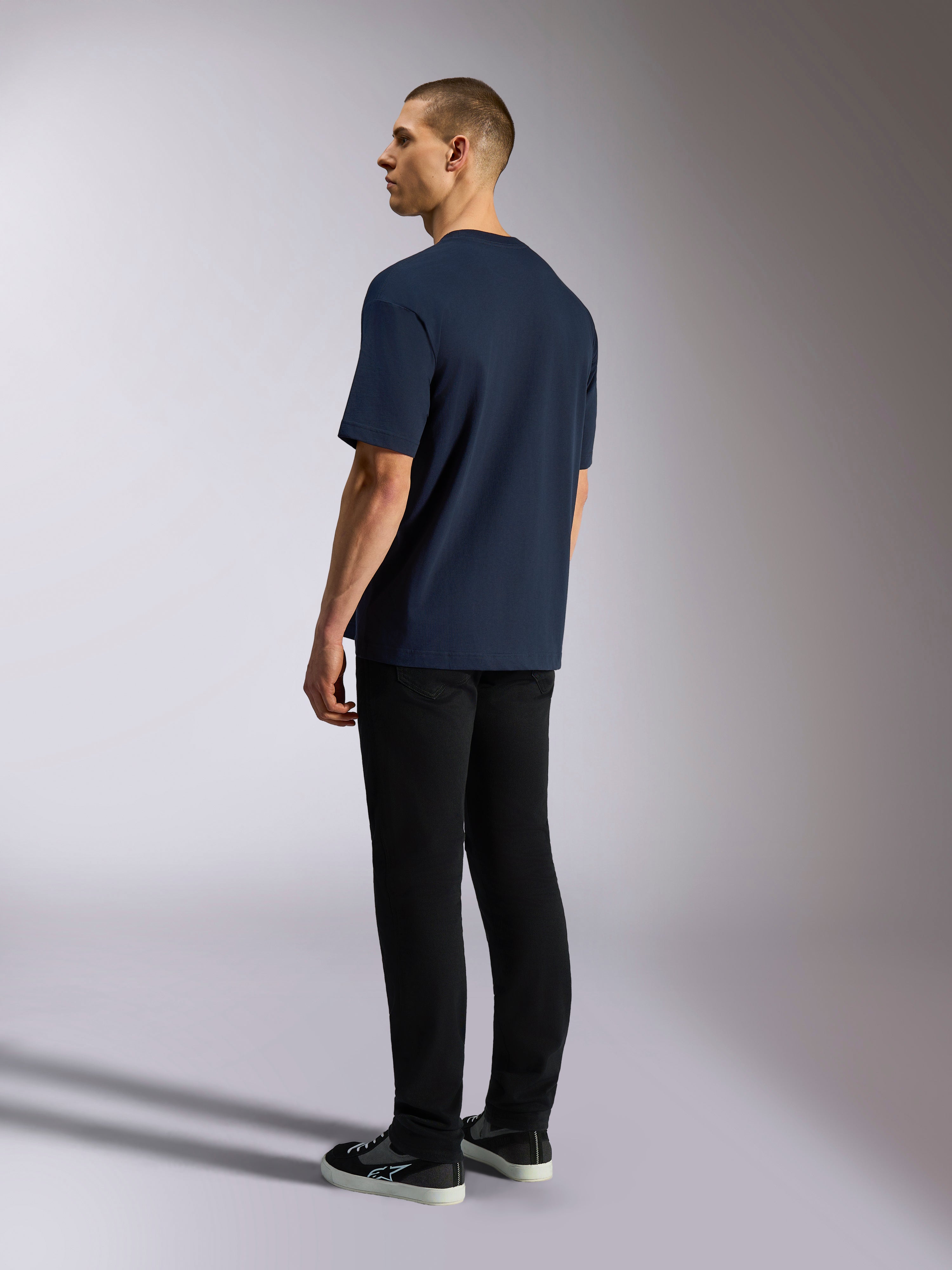 T-shirt Alpinestars Aplomb Oversized CSF, t-shirt à manches courtes, bleu marine, vue de dos sur mannequin, porté avec un pantalon noir et des baskets, streetwear décontracté d'inspiration sport automobile