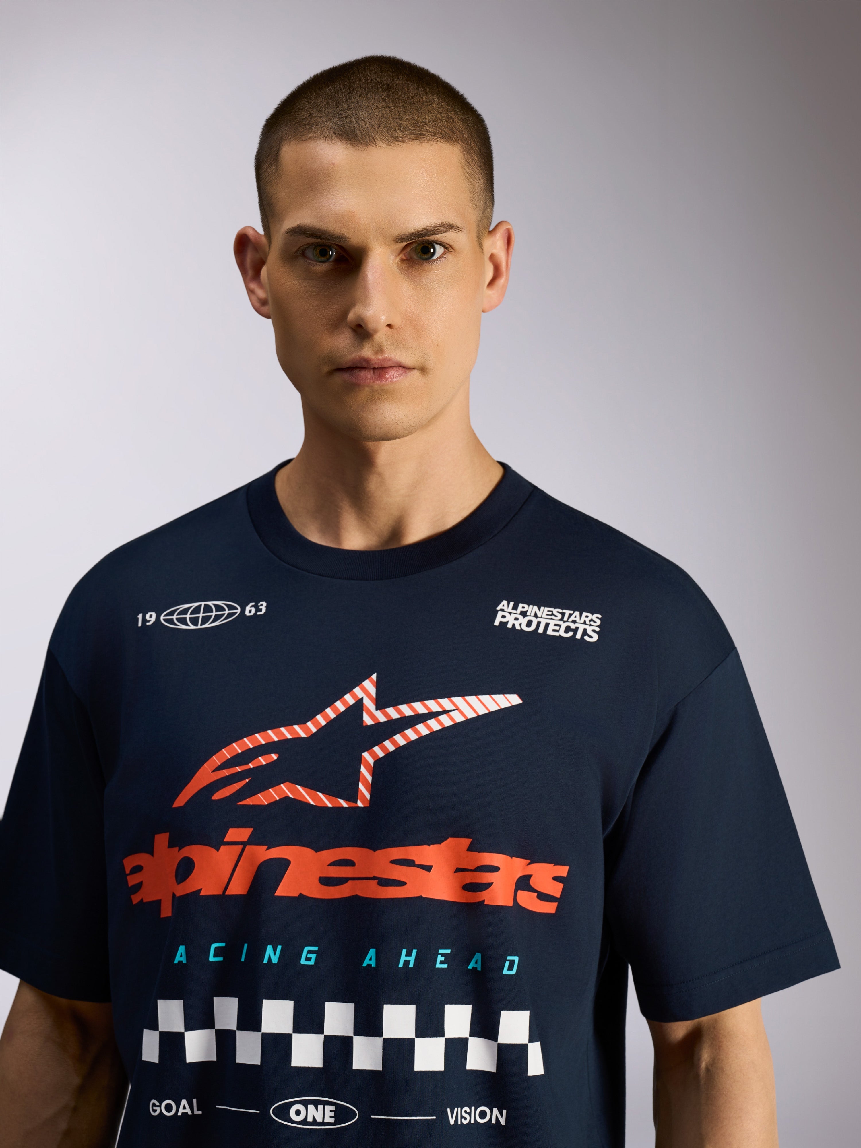 T-shirt surdimensionné Alpinestars Aplomb CSF, t-shirt à manches courtes, bleu marine, grand graphisme sur la poitrine avec logo rouge et motif à damier blanc, style streetwear motorsport décontracté