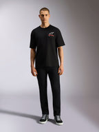 T-shirt Alpinestars Overhang Oversized CSF, t-shirt à manches courtes, noir, logo Astars blanc avec texte rouge, porté par un mannequin avec un pantalon noir et des baskets, style streetwear décontracté inspiré du sport automobile