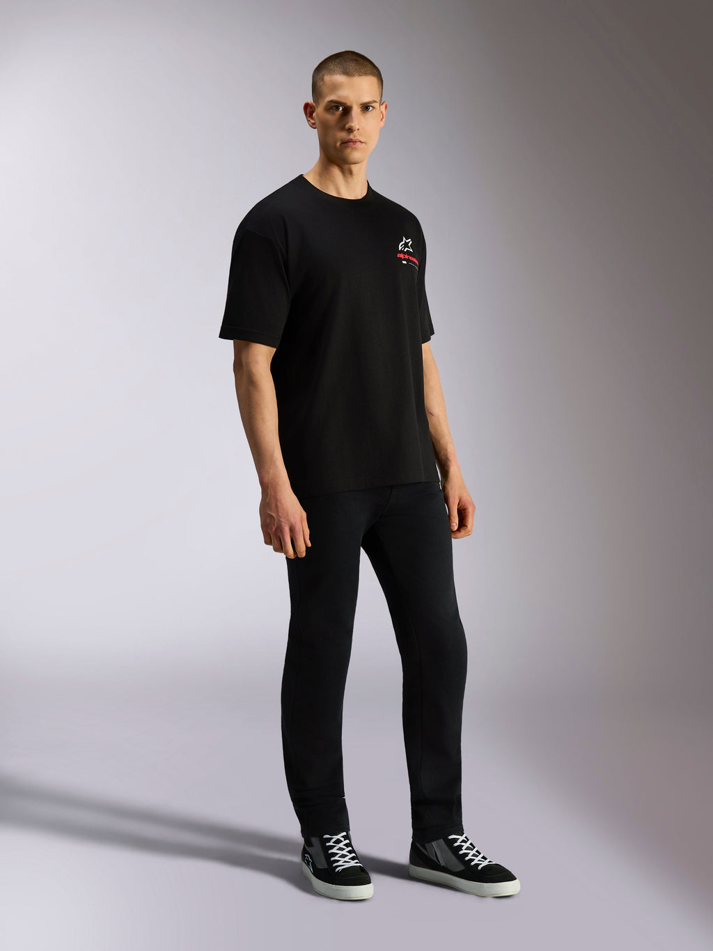 T-shirt Alpinestars Overhang Oversized CSF, manches courtes, noir, avec logo Astars blanc et rouge à l'avant, porté par un mannequin avec un pantalon noir et des baskets, design streetwear casual ample
