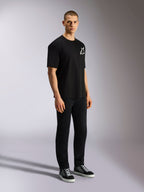 T-shirt Alpinestars One Oversized CSF, t-shirt à manches courtes, noir, logo Astars blanc sur la poitrine, coupe surdimensionnée, porté par un mannequin homme avec un pantalon noir et des baskets, streetwear décontracté d'inspiration motorsport