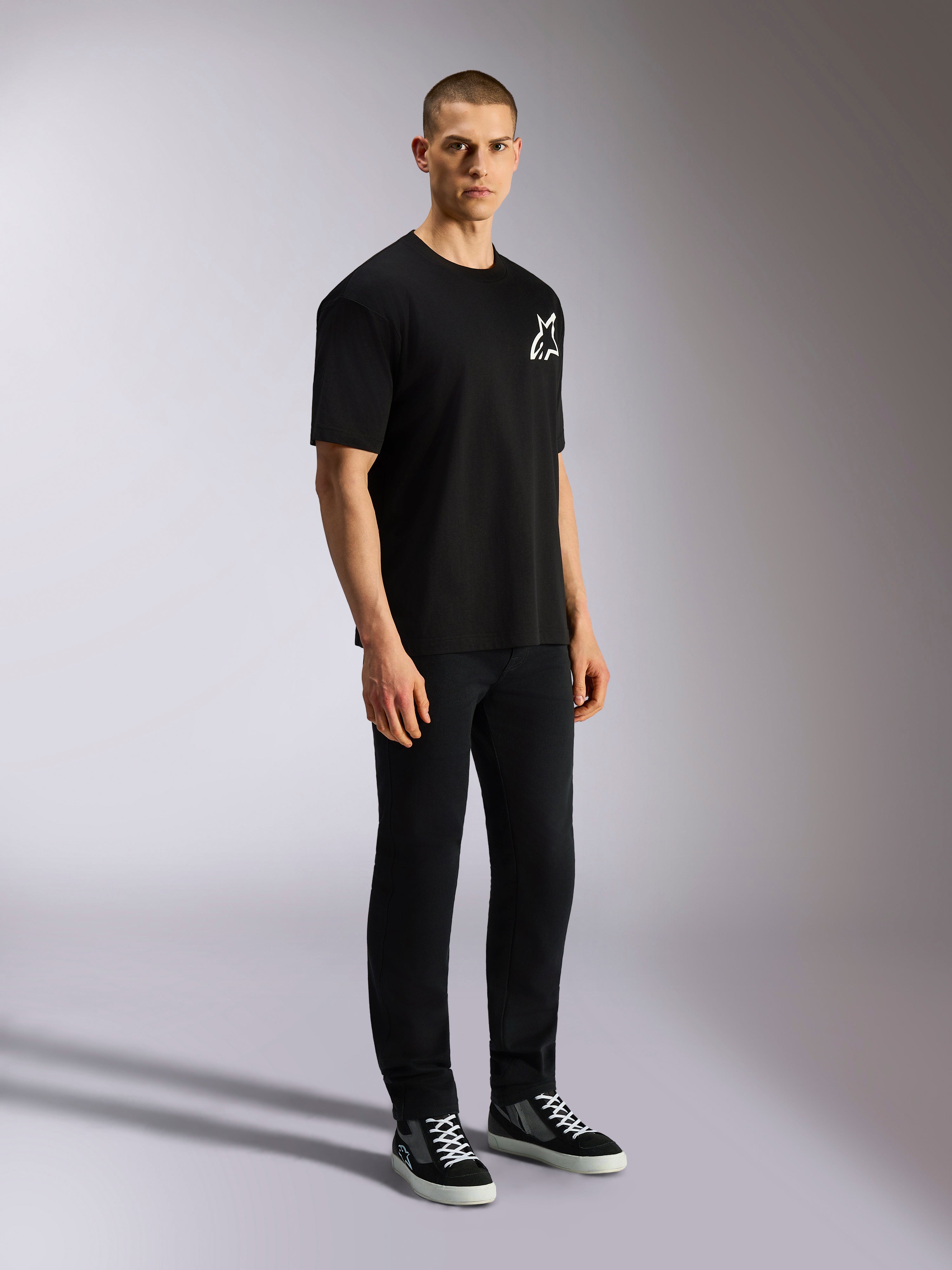 T-shirt Alpinestars One Oversized CSF, t-shirt à manches courtes, noir, logo Astars blanc sur la poitrine, coupe surdimensionnée, porté par un mannequin homme avec un pantalon noir et des baskets, streetwear décontracté d'inspiration motorsport