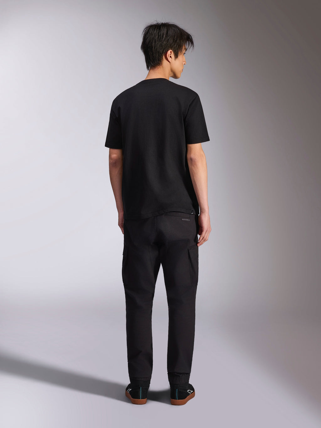 T-shirt Alpinestars Noka CSF, t-shirt à manches courtes, noir, vue de dos du mannequin portant le t-shirt avec un pantalon noir et des baskets, style streetwear décontracté motorsport
