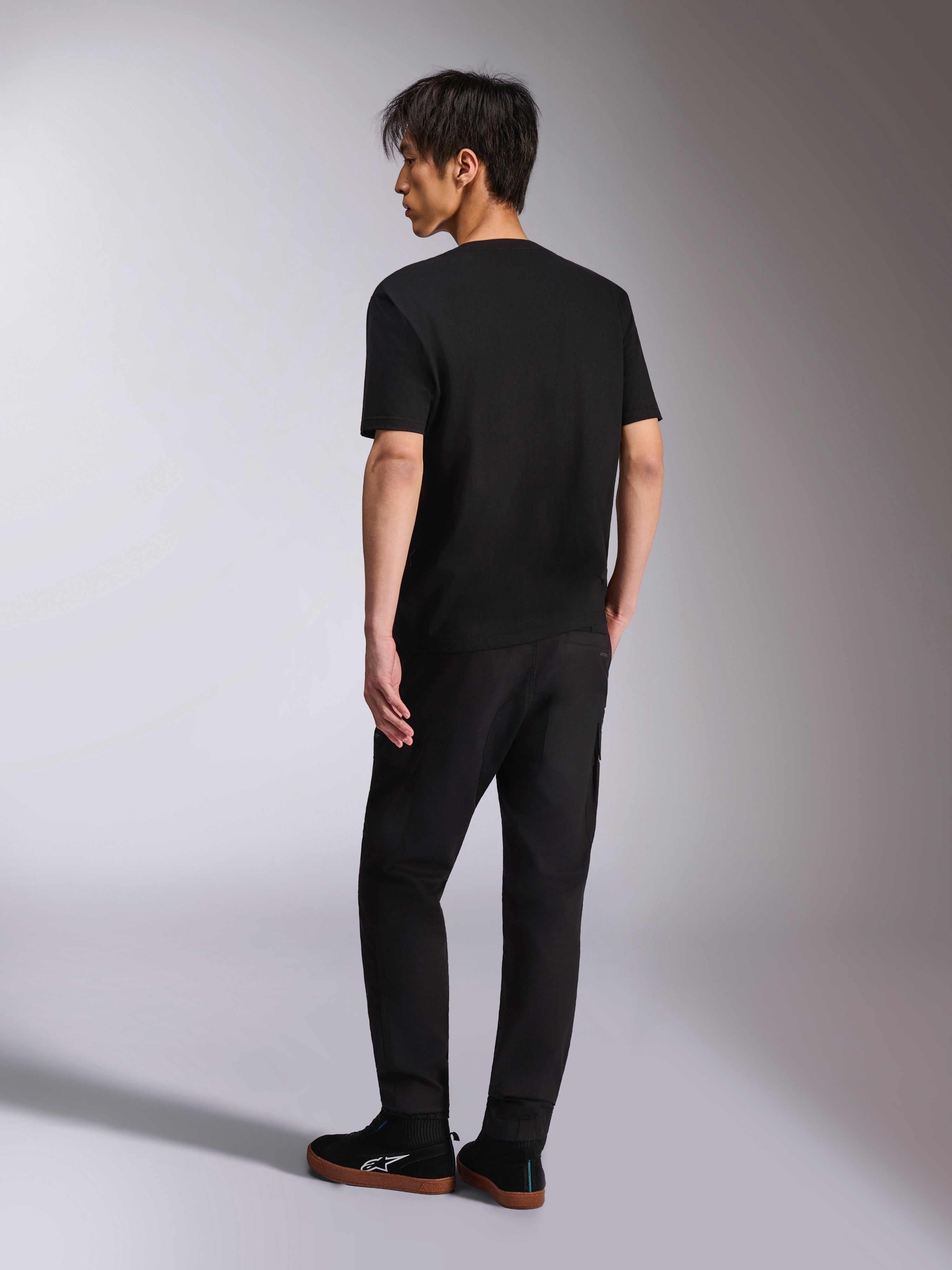 T-shirt Alpinestars Noka CSF, t-shirt à manches courtes, noir, vue de dos présentée sur un mannequin, associé à un pantalon noir et des baskets décontractées, streetwear de sport automobile minimaliste
