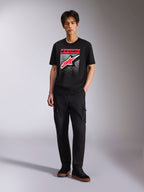 Alpinestars Noka CSF Tee, T-shirt à manches courtes, noir, logo Astars à l'avant avec graphique dégradé MX rouge et blanc, porté par un mannequin avec un pantalon cargo noir, streetwear motorsport décontracté