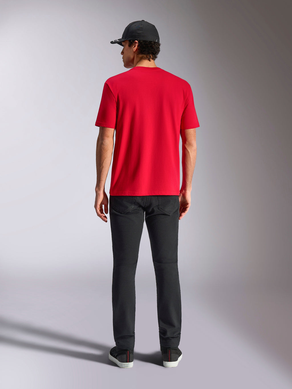 T-shirt Alpinestars Noka CSF, t-shirt à manches courtes, rouge, vue de dos, porté avec un pantalon noir et une casquette de baseball noire, streetwear décontracté inspiré du sport automobile