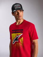 T-shirt Alpinestars Noka CSF, t-shirt à manches courtes, rouge, avec un logo Astars à l'avant avec dégradé MX jaune et rouge, porté avec une casquette Alpinestars 'Racing Ahead' noire, streetwear motorsport décontracté