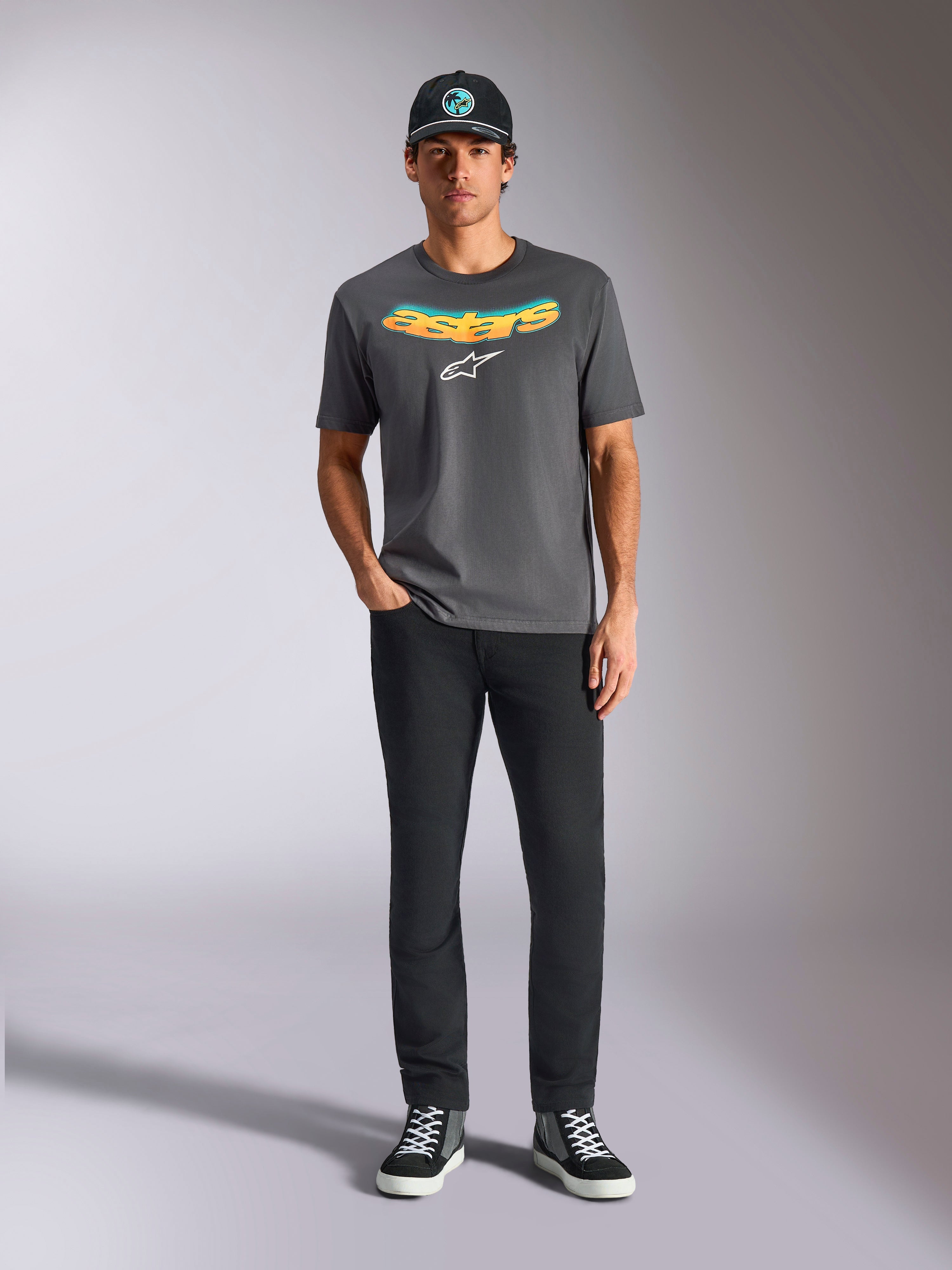Alpinestars Ellipsoid CSF Tee, Short Sleeve T-Shirt, Charcoal Gray, featuring a curved yellow and orange gradient wordmark and white Astars logo, worn by a model with black pants and a baseball cap, casual sportswear style