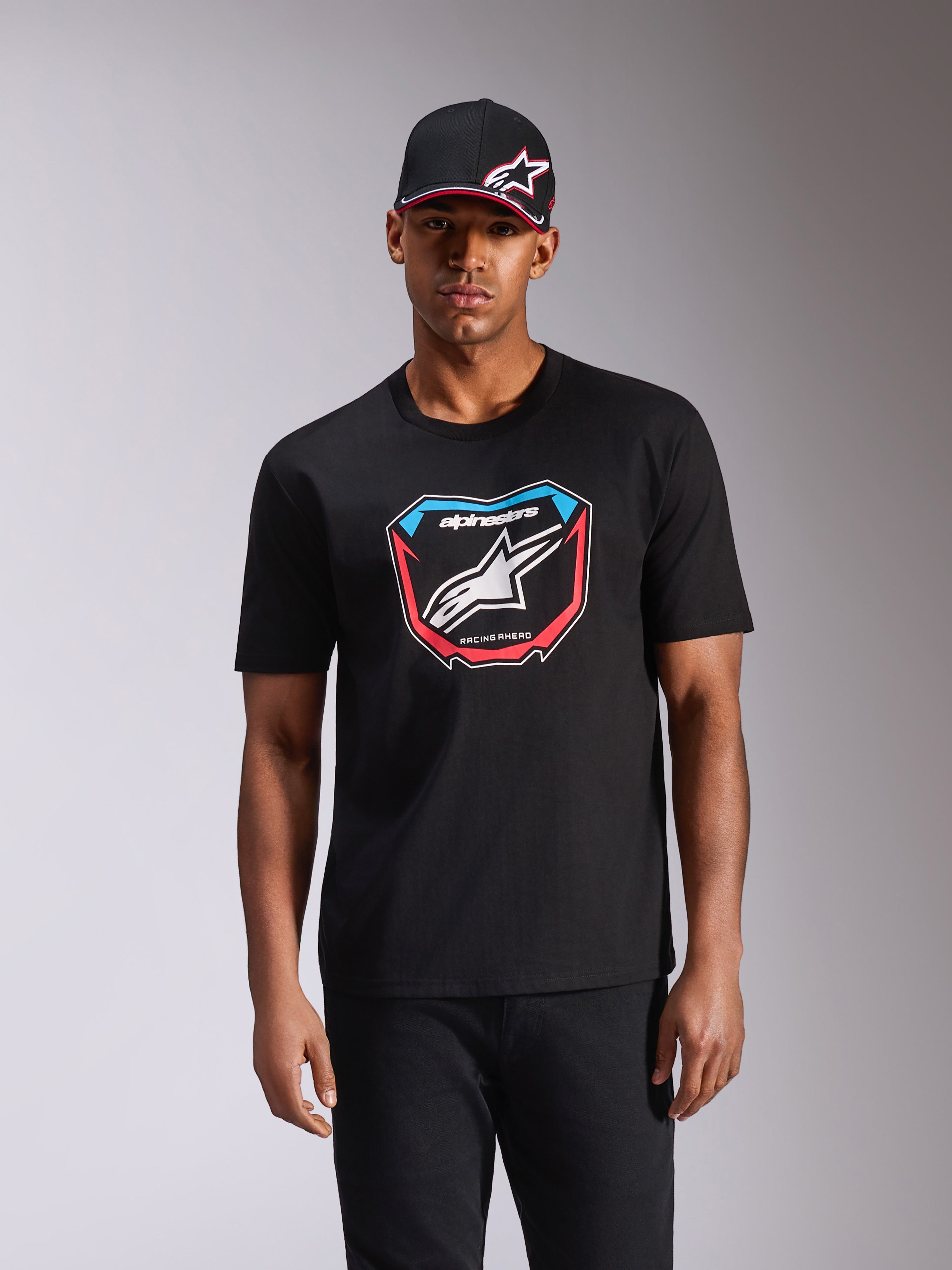 Alpinestars Plate CSF Tee, t-shirt à manches courtes, noir, avec graphique de plaque MX à l'avant, logo blanc et accents rouges et bleus, porté par un mannequin avec casquette noire assortie, style streetwear motorsport décontracté