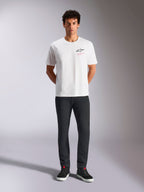 Alpinestars Pop Helmet CSF Tee, t-shirt à manches courtes, blanc, porté par un mannequin avec un pantalon noir et des baskets montantes noires, logo Astars à l'avant avec texte rose « Alpinestars Protects », streetwear motorsport décontracté