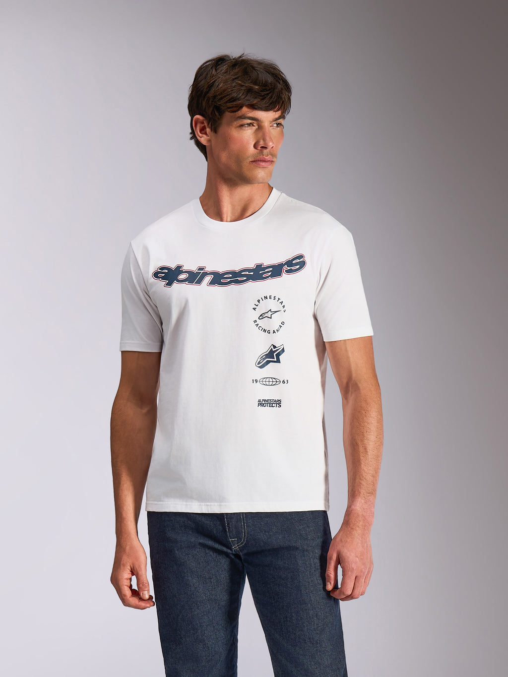 T-shirt Alpinestars Abus CSF, t-shirt à manches courtes, blanc, logo Alpinestars incurvé avec graphismes multiples empilés sur la poitrine, porté par un mannequin avec un jean en denim foncé, streetwear décontracté motorsport