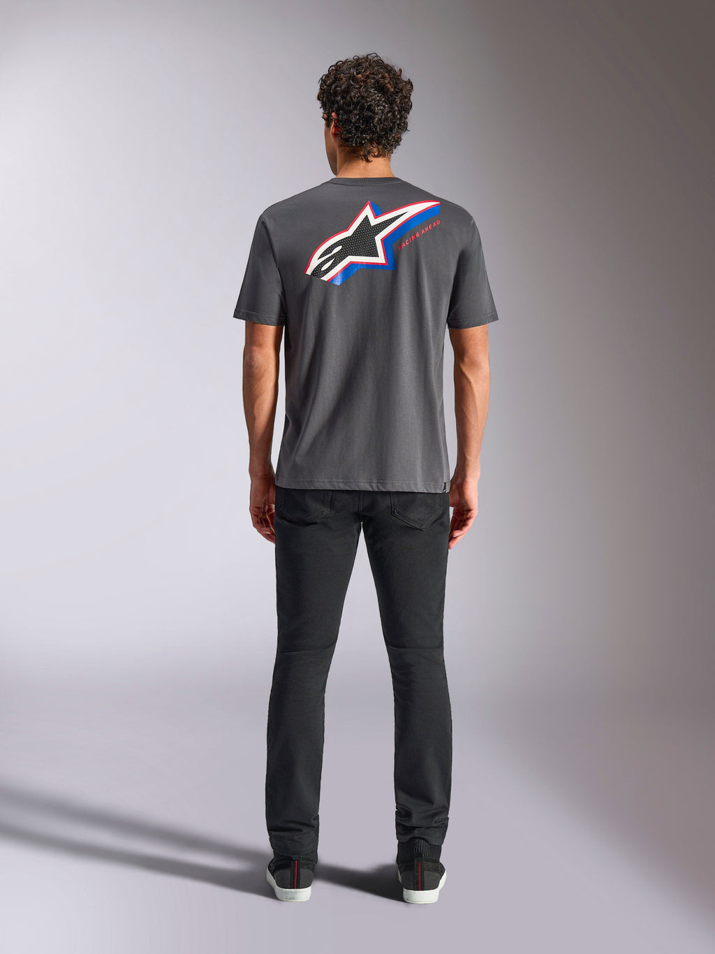 T-shirt Alpinestars Angler CSF, t-shirt à manches courtes, anthracite, grand logo Astars multicolore au dos avec des accents rouges et bleus, vue de dos sur modèle, streetwear décontracté inspiré du sport automobile
