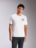 Alpinestars Order CSF Tee, t-shirt à manches courtes, blanc, motif sur la poitrine avec casque et palmiers, porté par un mannequin avec un pantalon sombre, streetwear décontracté inspiré des sports mécaniques