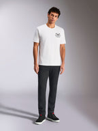 Alpinestars Order CSF Tee, t-shirt à manches courtes, blanc, petit graphisme noir sur la poitrine avec casque et palmiers, streetwear décontracté inspiré du sport automobile, porté par un mannequin avec un pantalon noir et des baskets