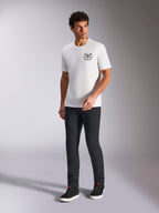Alpinestars Order CSF Tee, t-shirt à manches courtes, blanc, logo avec casque et palmiers, porté avec un pantalon noir et des baskets montantes, streetwear décontracté motorsport