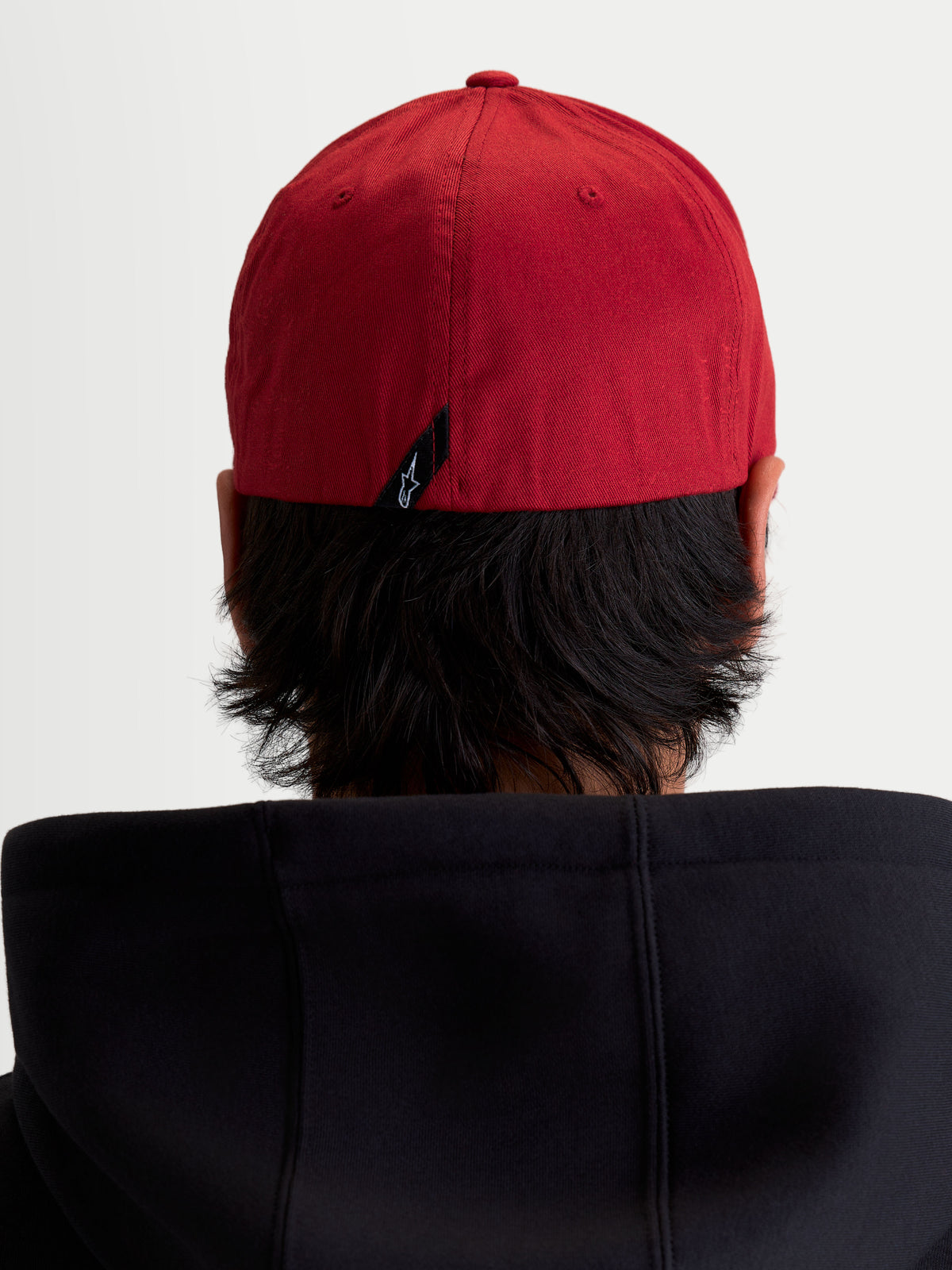 Alpinestars Casquette Pivot, casquette de baseball sportswear rouge foncé, vue arrière sur modèle montrant la construction à dos flexible et une petite étiquette avec le logo Astars à l'arrière.