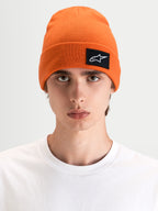 Alpinestars Bonnet Augment Cuff, bonnet sportswear orange vif, porté par un modèle dans une silhouette à coupe profonde avec un écusson logo Astars tissé