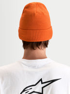 Alpinestars Bonnet Augment Cuff, bonnet en maille orange avec une coupe profonde et un design à revers, vue de dos sur un modèle portant un t-shirt blanc avec un logo Astar noir