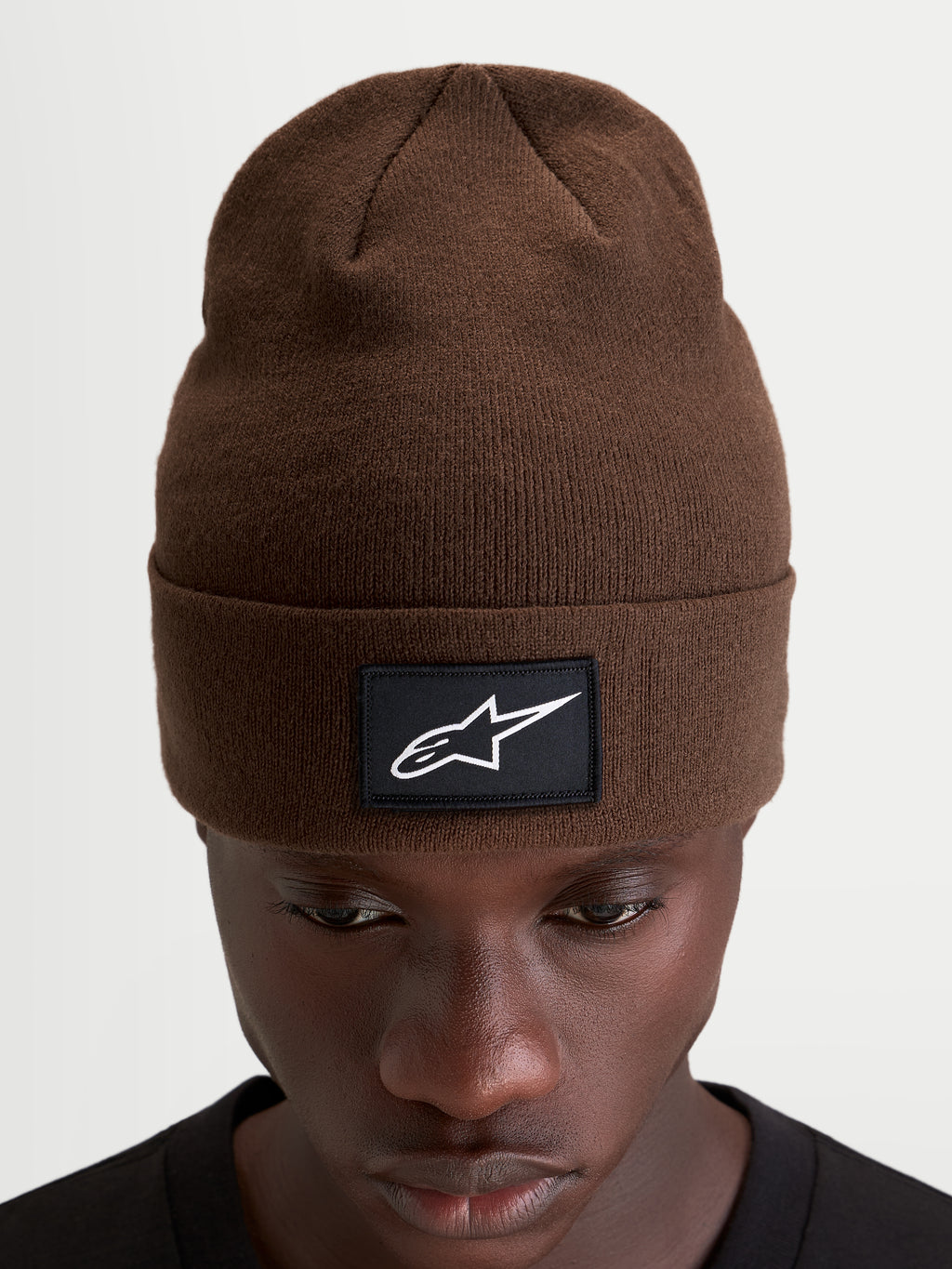 Bonnet Augment Cuff d'Alpinestars, bonnet sportswear marron avec écusson noir et blanc du logo Astars, coupe profonde portée sur un modèle