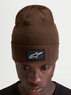 Bonnet Augment Cuff d'Alpinestars, bonnet sportswear marron avec écusson noir et blanc du logo Astars, coupe profonde portée sur un modèle