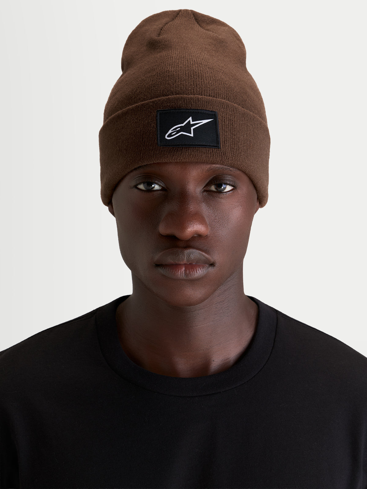 Alpinestars Bonnet Augment Cuff, bonnet sportswear marron avec un écusson tissé du logo sur le revers, porté par un modèle portant un t-shirt noir