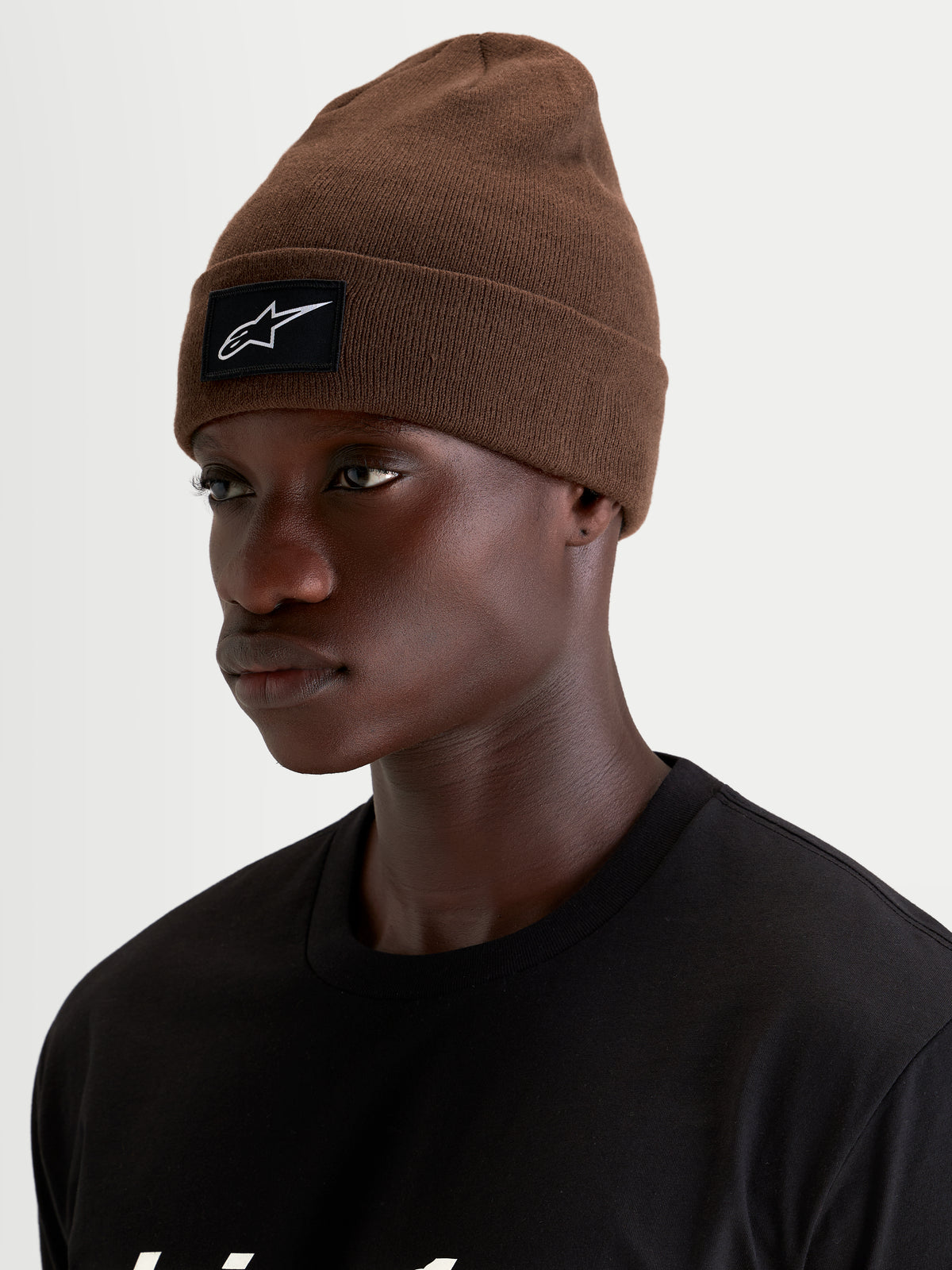 Alpinestars Bonnet Augment Cuff, bonnet sportswear marron en maille tricotée avec écusson tissé du logo noir et blanc sur le revers, porté par un modèle