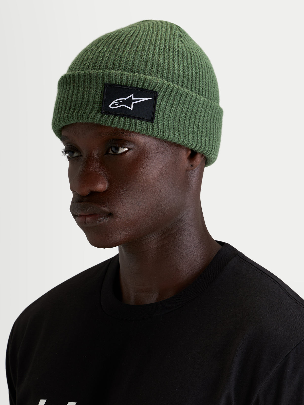 Bonnet Unload Rib Cuff d'Alpinestars, bonnet casual vert pois porté par un modèle, avec maille jersey tricotée et écusson tissé SAstars noir et blanc