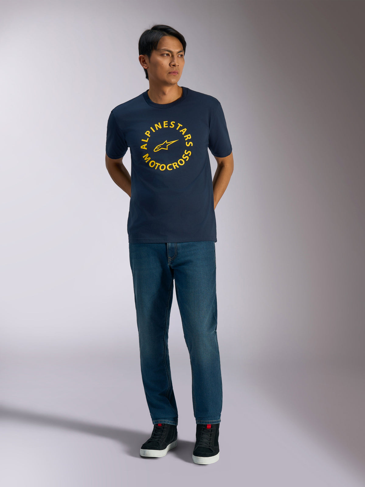 Alpinestars MX CSF Tee, t-shirt à manches courtes, bleu marine, avec un graphique circulaire jaune Alpinestars Motocross, porté par un mannequin avec un jean bleu et des baskets noires, style streetwear décontracté motorsport