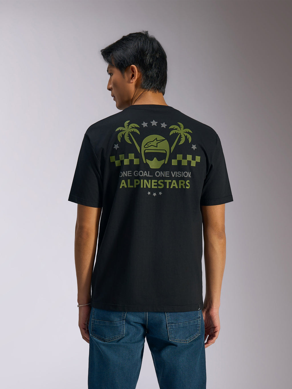 Alpinestars Order CSF Tee, t-shirt à manches courtes, noir, vue de dos, graphisme vert olive avec palmiers et logo de casque, texte 'ONE GOAL. ONE VISION. ALPINESTARS', porté avec un jean bleu, style streetwear décontracté