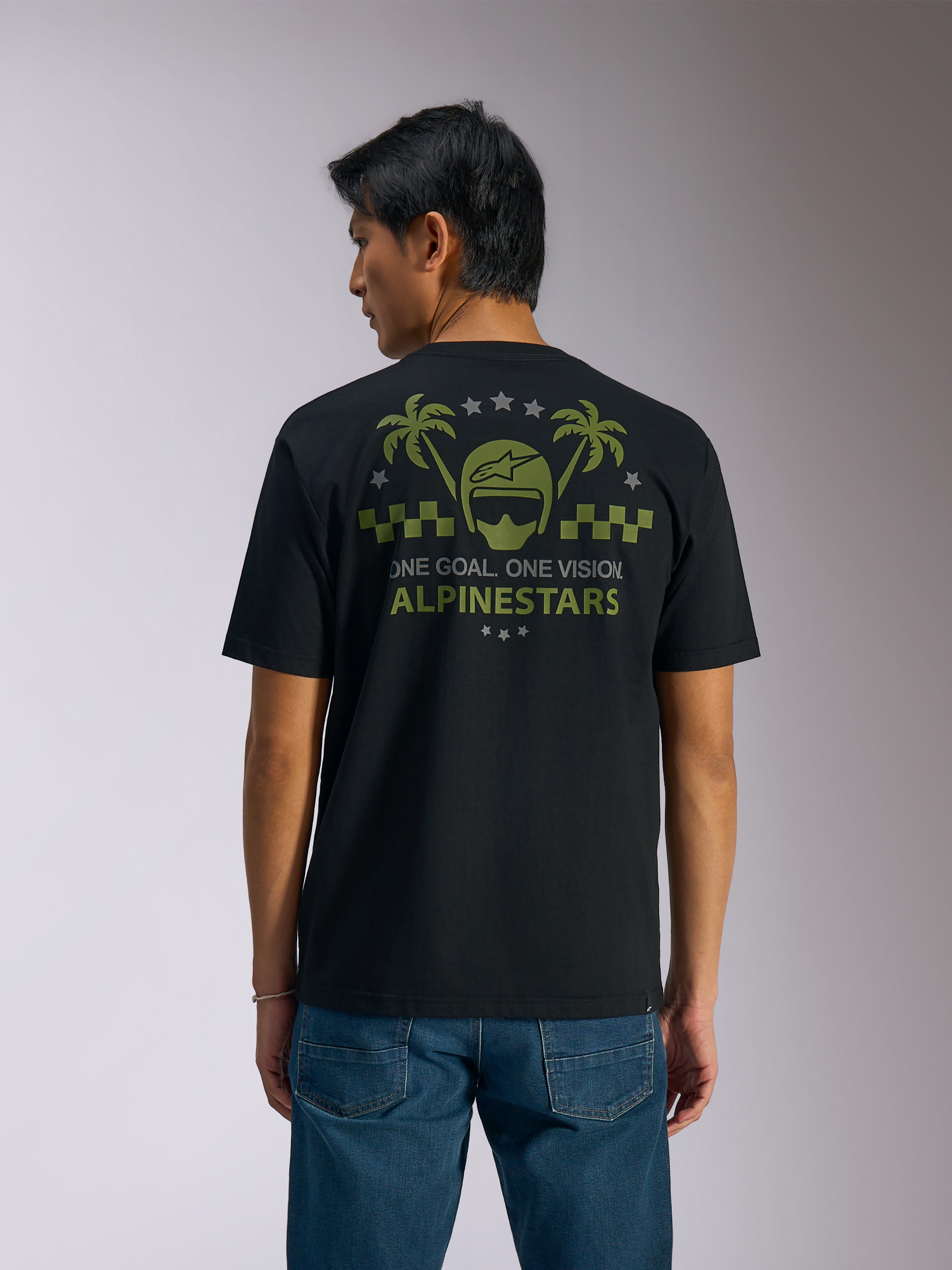 Alpinestars Order CSF Tee, t-shirt à manches courtes, noir, vue de dos, graphisme vert olive avec palmiers et logo de casque, texte 'ONE GOAL. ONE VISION. ALPINESTARS', porté avec un jean bleu, style streetwear décontracté