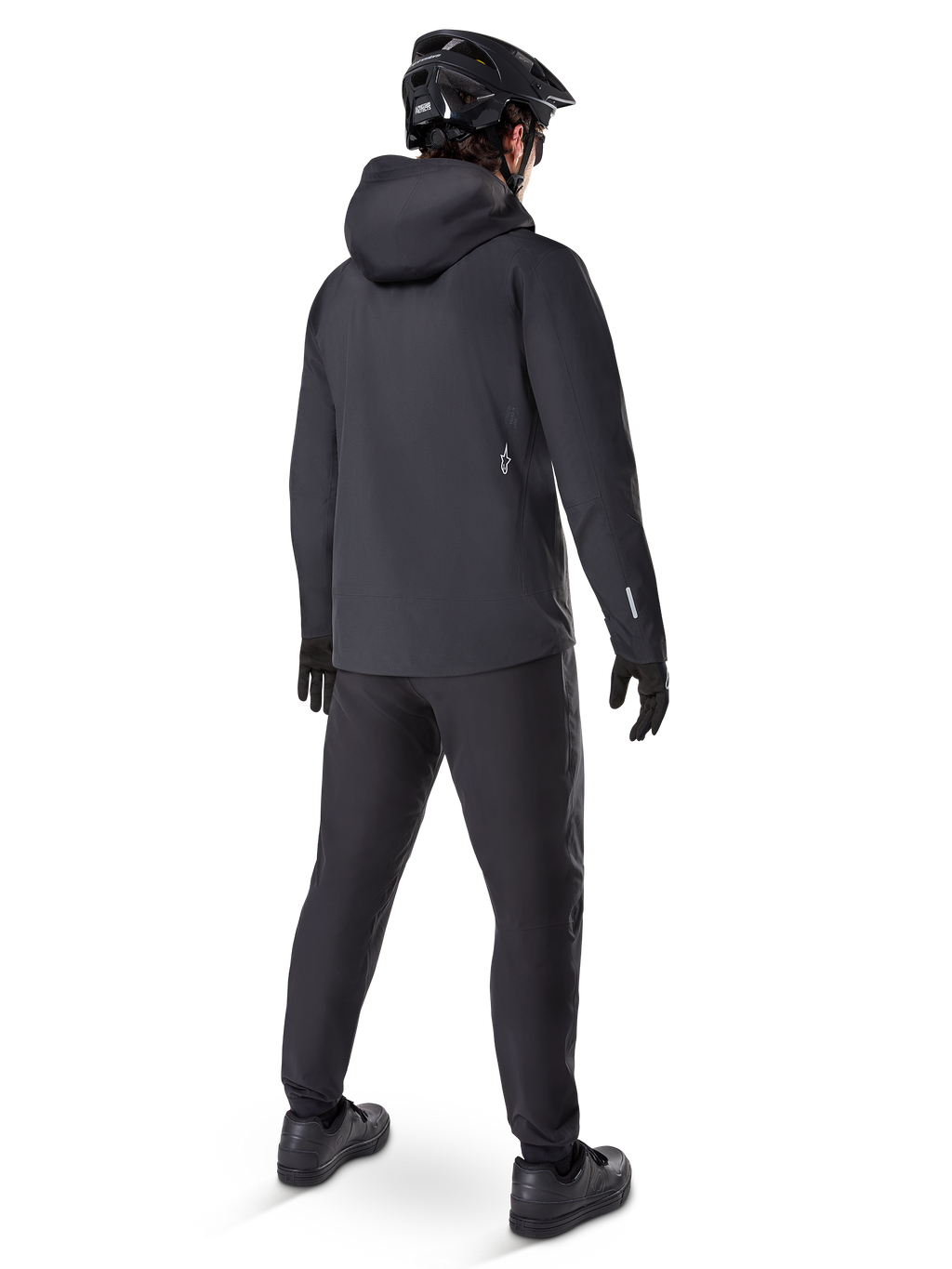 Veste imperméable Alpinestars A-Dura Elite, noire, vue de dos montrant la capuche par-dessus le casque et l'ourlet arrière plus long, associée à un pantalon de VTT, des gants et un casque noirs assortis pour une protection complète sur les sentiers par tous les temps.