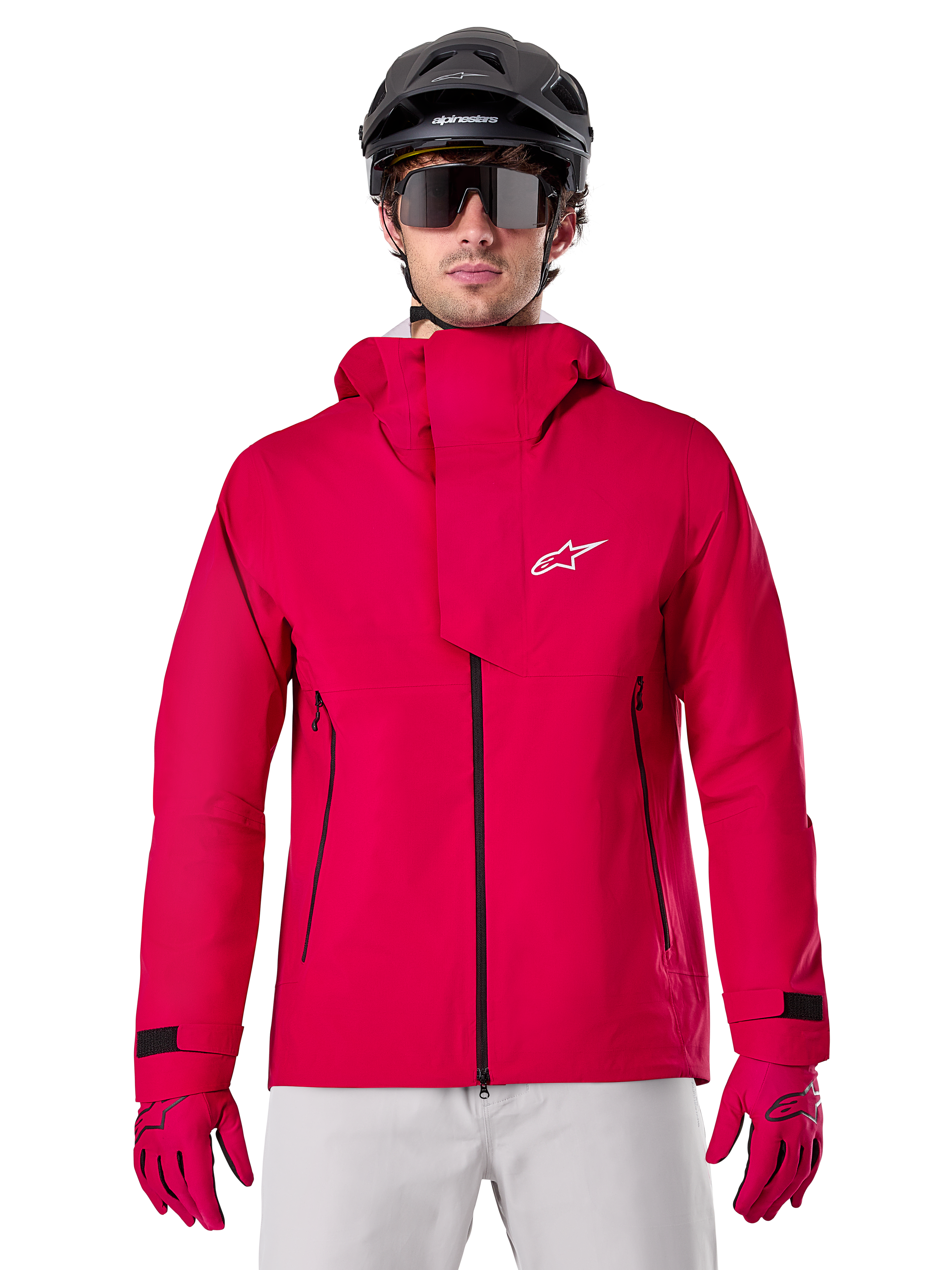 Alpinestars A-Dura Elite Waterproof Jacket, veste de pluie pour VTT, rouge fluo, col montant avec logo Alpinestars blanc, fermetures éclair noires, portée avec gants assortis et casque de vélo noir, équipement de cyclisme technique imperméable