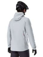 Veste thermique Alpinestars A-Dura, Gris Titanium, vue de dos d'un cycliste portant la veste isolante à capuche, associée à un casque de VTT noir et des gants noirs, avec un petit logo Alpinestars en bas du dos, conçue pour le VTT par temps froid.