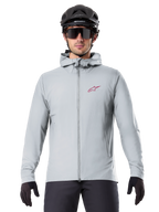 Veste thermique Alpinestars A-Dura en Titanium, veste de cyclisme à capuche gris clair avec logo étoile rouge sur la poitrine, portée par un cycliste avec casque de VTT noir, lunettes de soleil et gants, équipement isolé pour le VTT