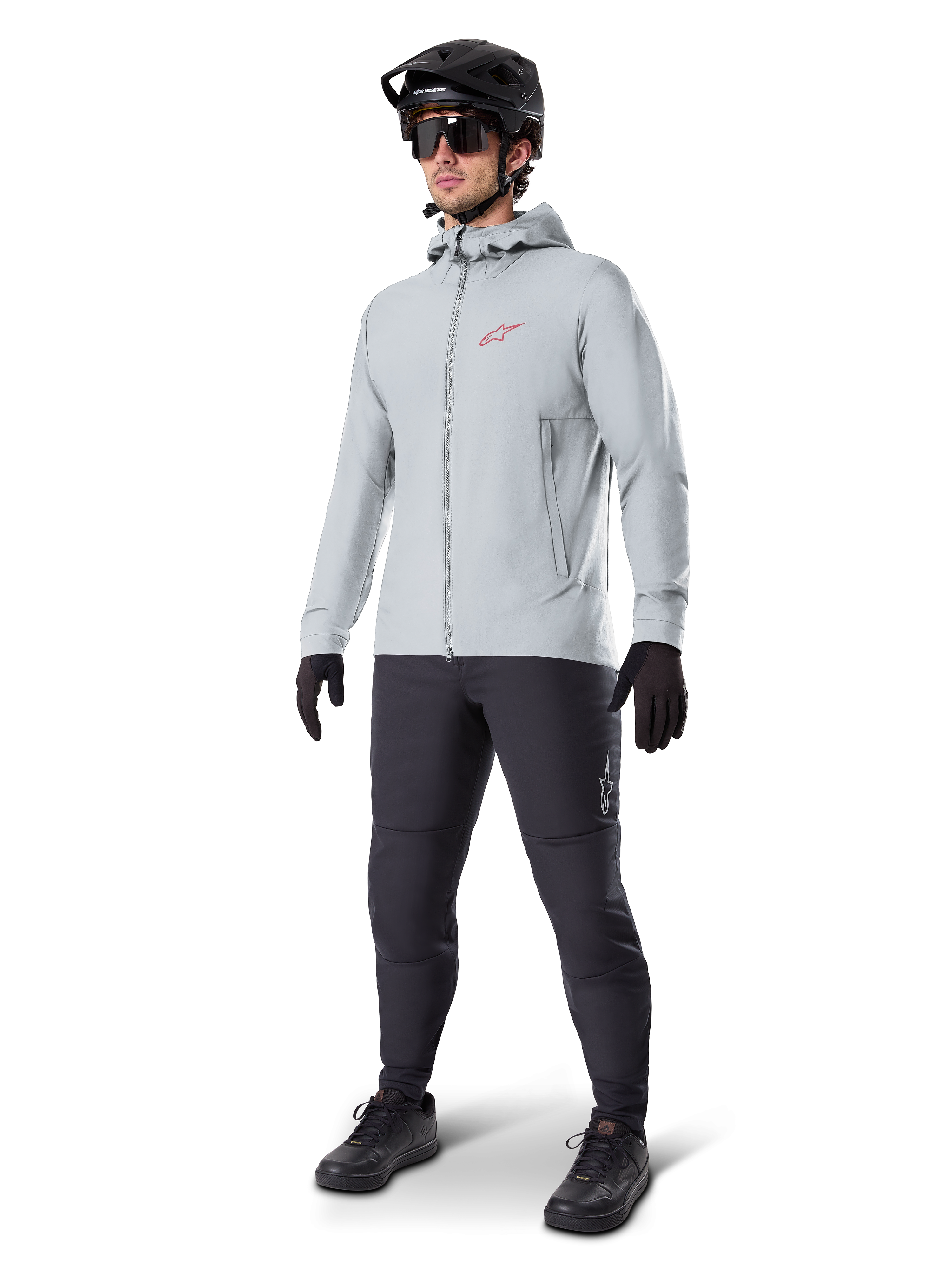 Veste thermique Alpinestars A-Dura en Titanium, veste de cyclisme à capuche gris clair avec logo Alpinestars rouge sur la poitrine, portée par un homme avec casque de VTT noir, lunettes de soleil, pantalon gris foncé et gants noirs, équipement de VTT professionnel