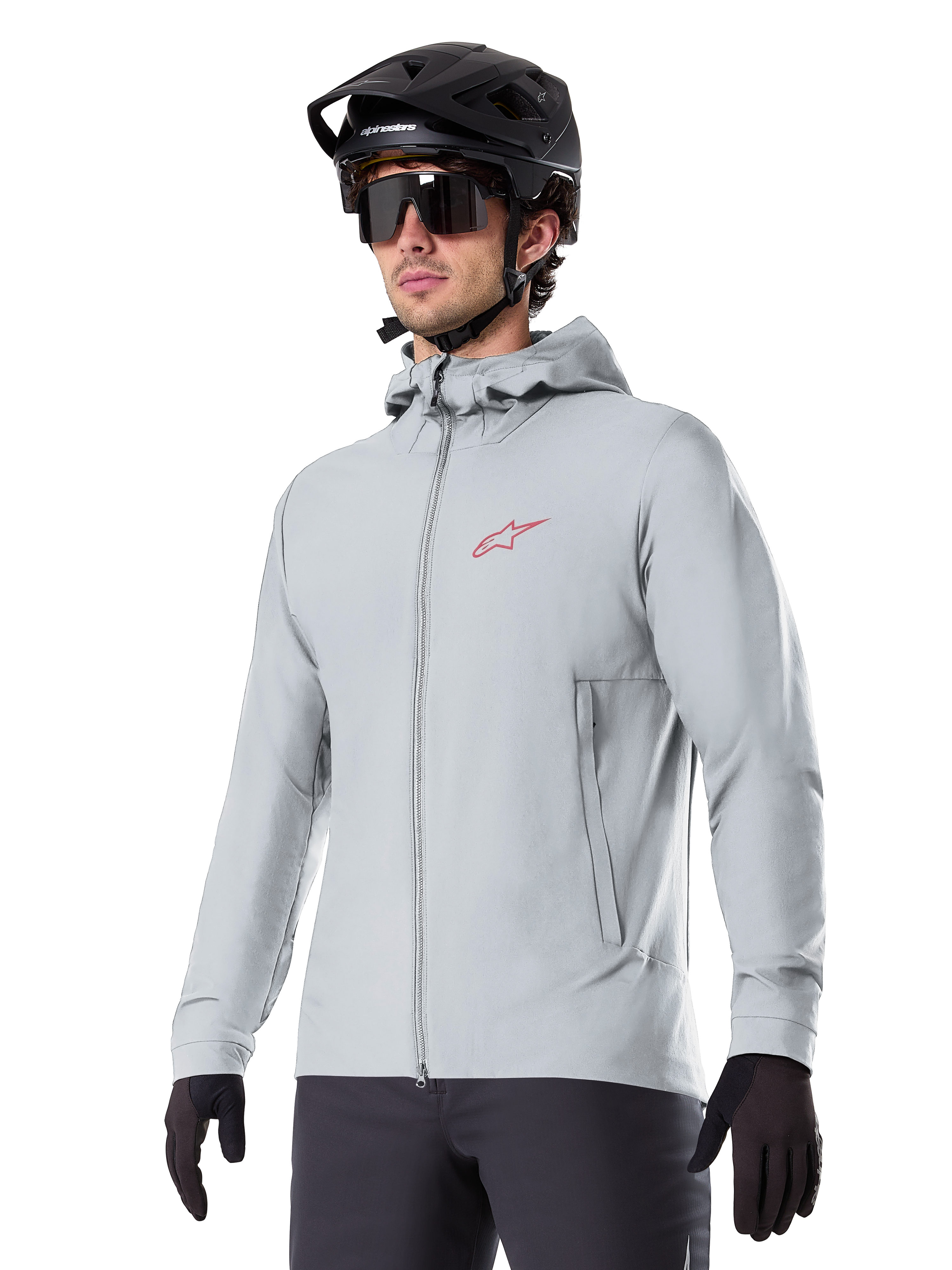 Veste thermique Alpinestars A-Dura, veste de cyclisme isolante gris clair, design à capuche avec petit logo rouge, portée avec un casque et des gants noirs, vêtement technique de VTT pour rouler par temps froid