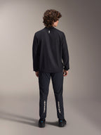 Veste coupe-vent Alpinestars A-Aria, noire, vue de dos, veste de cyclisme légère et résistante au vent avec un petit logo blanc sur le haut du dos, portée avec un pantalon noir assorti arborant le marquage vertical Alpinestars sur les mollets, équipement de VTT haute performance
