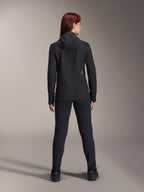 Woman wearing Alpinestars Stella A-Dura Thermal Jacket, back view, black insulated cycling jacket with hood, matching black pants and shoes, featuring a small white logo on the lower back