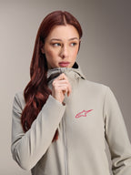 Alpinestars Woman Stella A-Dura Thermal Jacket, Titanium gray with a pink Alpinestars star logo, model with long red hair wearing and zipping up the hooded jacket, lightweight insulated cycling apparel for cold weather.