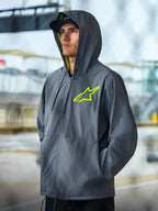 Veste coupe-vent Alpinestars Speeder Chromium, veste lifestyle gris anthracite avec accents jaune haute visibilité, modèle à capuche avec doublure intérieure jaune et logo sur la poitrine, vêtement streetwear décontracté porté par un mannequin en extérieur