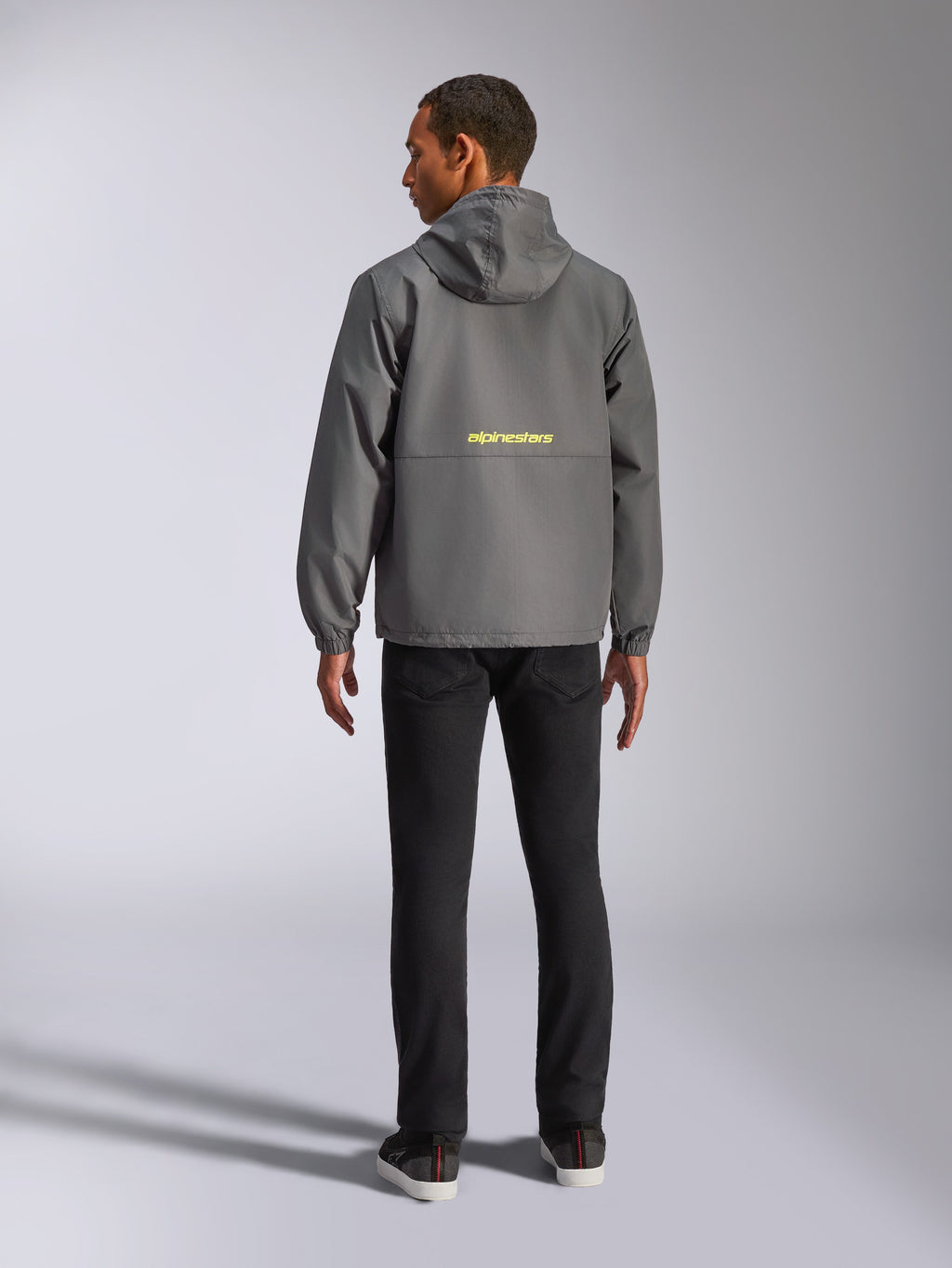 Veste coupe-vent Alpinestars Speeder Chromium, gris anthracite et jaune haute visibilité, vue de dos montrant le logo Alpinestars jaune au centre, coupe-vent léger avec capuche et poignets élastiques, streetwear décontracté d'inspiration motorsport