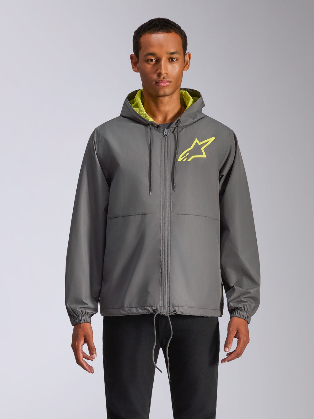 Alpinestars Speeder Chromium Windbreak Jacket, coupe-vent à capuche gris anthracite avec logo étoile jaune fluo, intérieur de capuche vert citron, poignets élastiques, cordons de serrage réglables, fermeture éclair frontale, style motorsport décontracté