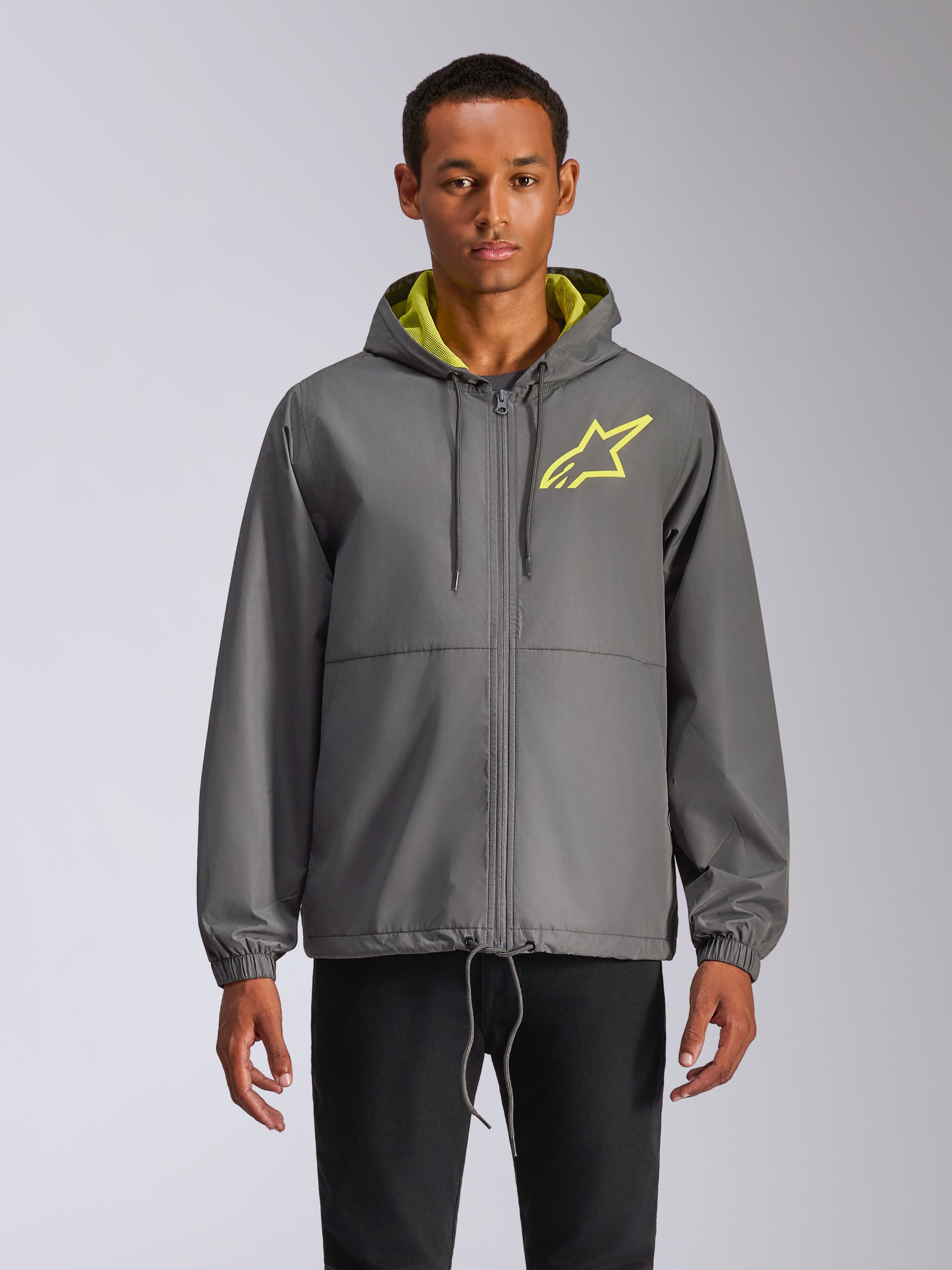 Alpinestars Speeder Chromium Windbreak Jacket, coupe-vent à capuche gris anthracite avec logo étoile jaune fluo, intérieur de capuche vert citron, poignets élastiques, cordons de serrage réglables, fermeture éclair frontale, style motorsport décontracté