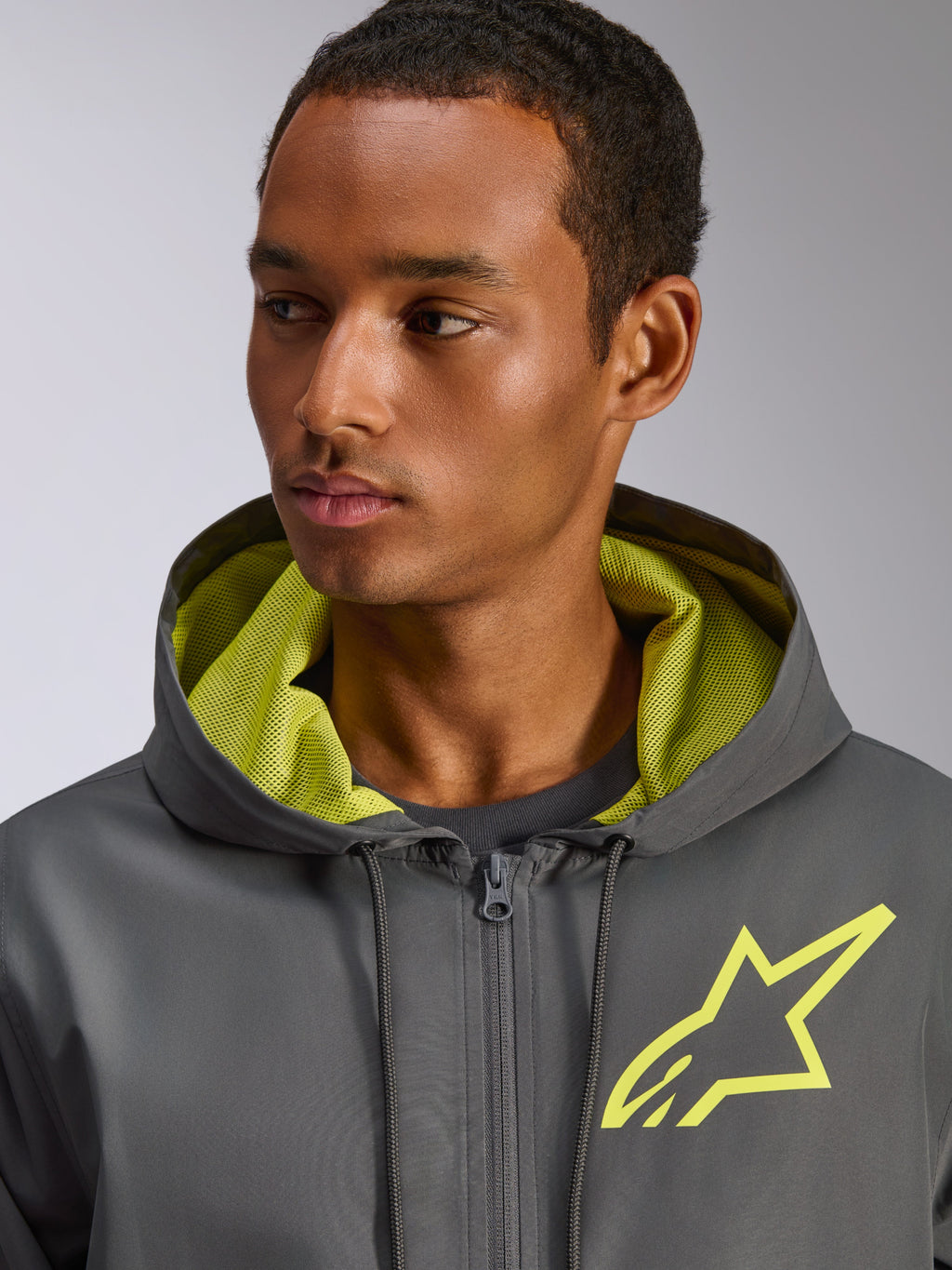 Veste coupe-vent Alpinestars Speeder Chromium, gris anthracite avec des accents jaune fluo, logo étoile jaune sur la poitrine et doublure de capuche en mesh assortie, coupe-vent léger décontracté