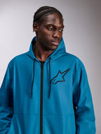 Modèle masculin portant la veste coupe-vent Alpinestars Speeder Chromium, bleue, coupe-vent léger à capuche, logo Astars noir sur la poitrine, fermeture éclair frontale et cordons de serrage noirs, streetwear décontracté d'inspiration sport automobile
