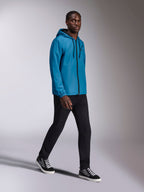 Veste coupe-vent Alpinestars Speeder Chromium, coupe-vent à capuche bleu porté par un mannequin homme, avec fermeture éclair frontale noire et logo sur la poitrine, assorti à un pantalon noir et des baskets montantes, tenue de sport décontractée inspirée par le sport automobile