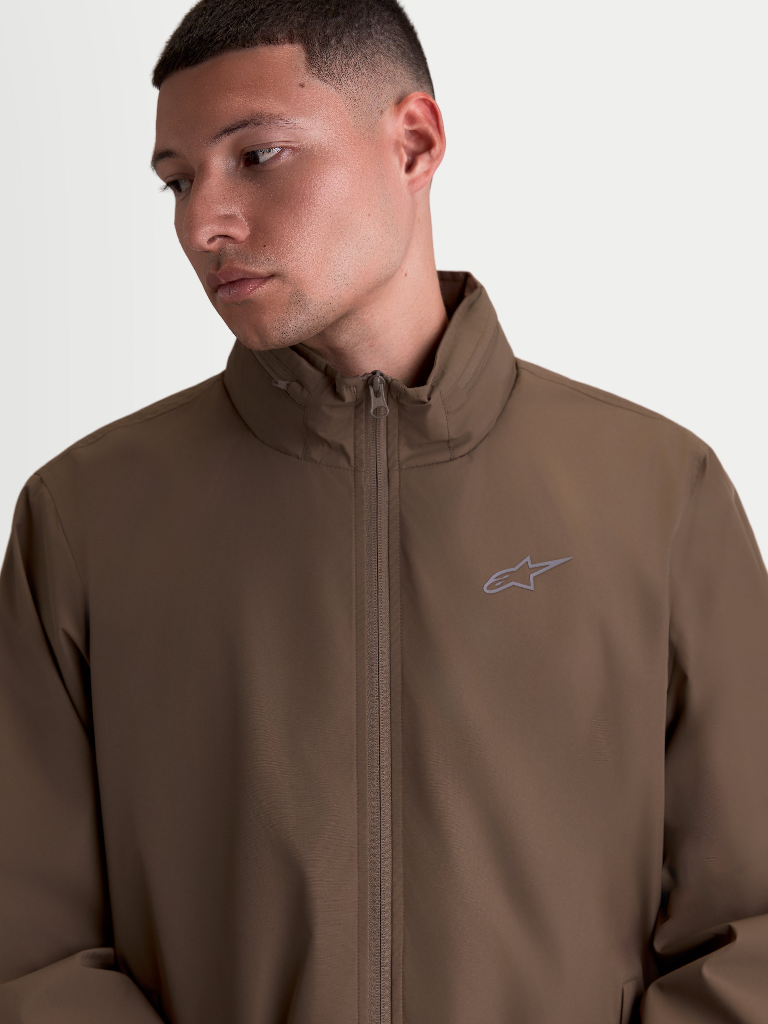Alpinestars Veste Overhaul Racer, veste de sportswear légère pour homme, marron, dotée d'un col montant avec compartiment pour capuche dissimulée et petit logo Astars sur la poitrine, style inspiré du sport automobile.